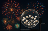 Eine Trommel mit Lottokugeln vor einem dunklen Himmel mit einem Feuerwerk.