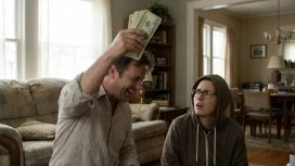 Ein Mann hält jubelnd ein Bündel Geldscheine in die Höhe, während eine weitere Person neben ihm überrascht und fragend auf ihn blickt.