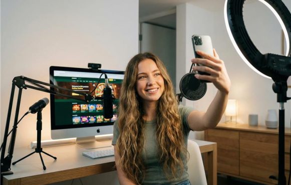 Eine KI-Influencerin nimmt ein Selfie auf. Im Hintergrund ist eine Glücksspielseite auf ihrem Computer geöffnet.