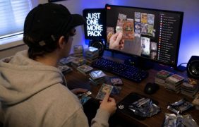 Ein Mann schaut einen Livestream, in dem Trading Cards geöffnet werden. Vor ihm liegen verschiedene Stapel mit Trading Cards.