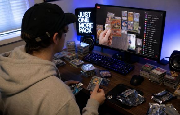 Ein Mann schaut einen Livestream, in dem Trading Cards geöffnet werden. Vor ihm liegen verschiedene Stapel mit Trading Cards.