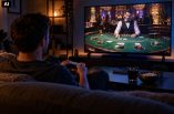 Ein Mann spielt auf der Konsole. Im Spiel besucht er gerade ein realistisch wirkendes Casino.